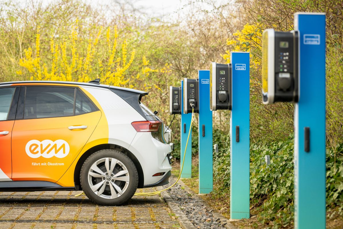 Ein Elektroauto mit EVM-Branding lädt an einer Reihe von Ladestationen im Freien.