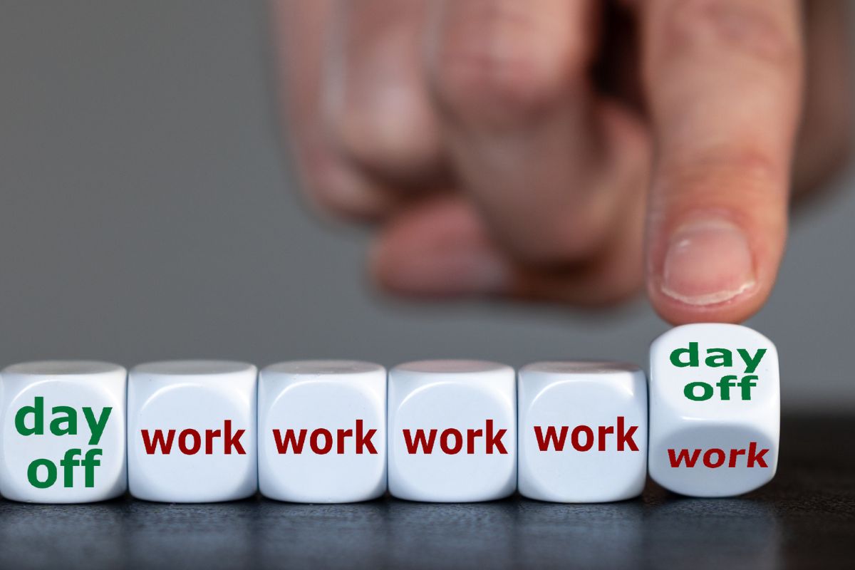 Reihe von 6 Würfeln. 1er mit der Aufschrift "Day off" und 5 mit der Aufschrift "Work" der letzte Würfel wird von einer Hand umgestoßen, und man sieht bereits die neue Seite mit der Aufschrift " day off".