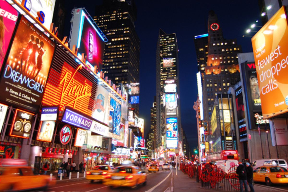 Times Square bei Nacht mit leuchtenden Werbetafeln und vorbeifahrenden gelben Taxis.