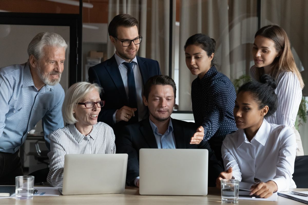 Sinnbild zum Thema Generationenkonflikt. Jüngere Mitarbeitende bringen älteren den Computer näher.