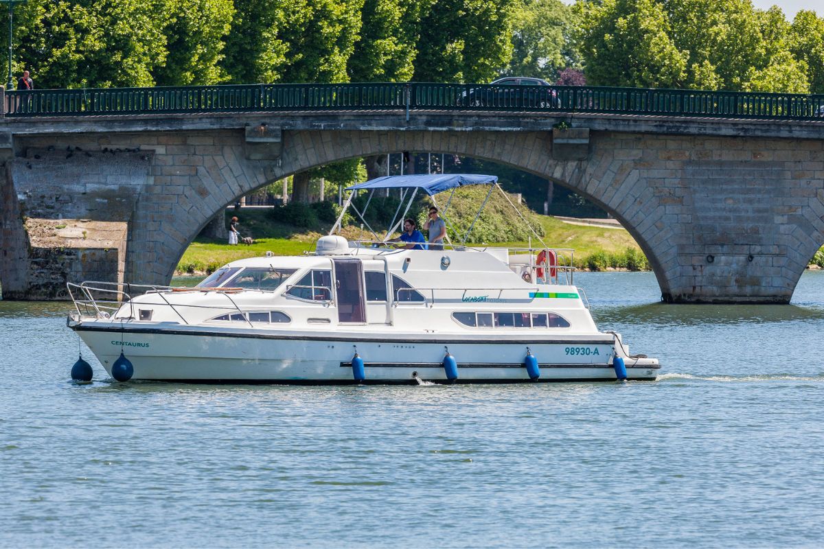 Ein Hausboot schippert auf einem Fluss bei Sonnenschein.