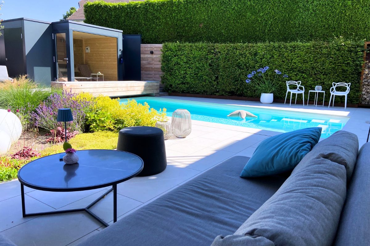 Eine Gartenanlage bei Sonnenschein inklusive Pool, Rasenfläche und Sitzmöglichkeiten.