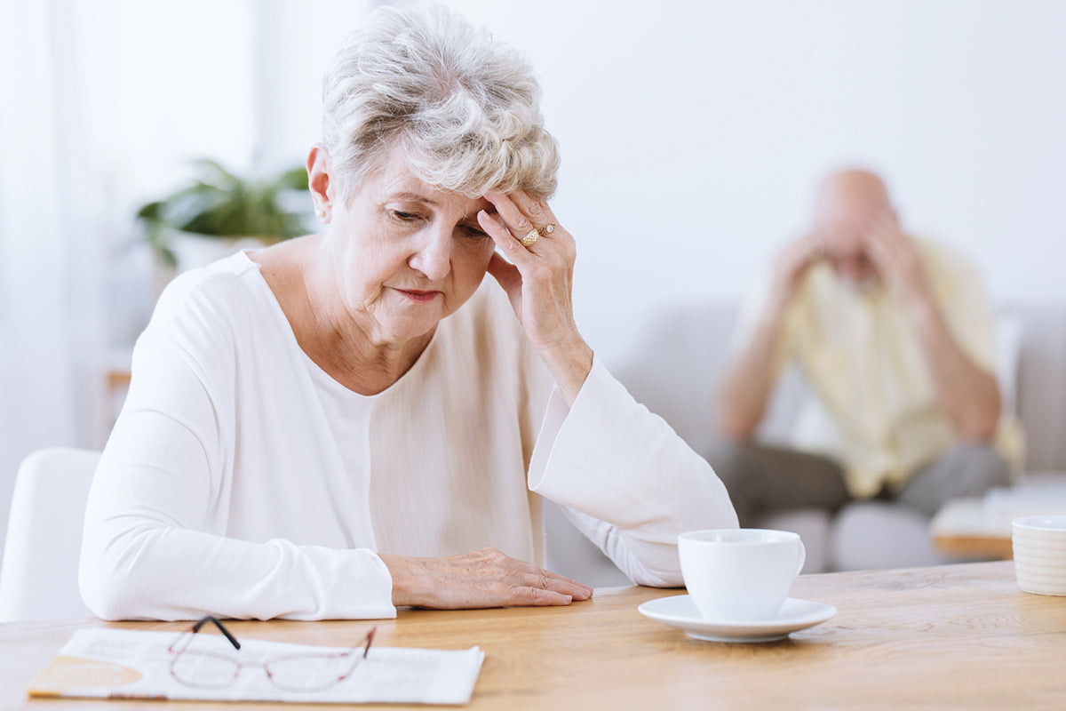 Eine ältere Frau sitzt nachdenklich an einem Tisch und sieht traurig aus.