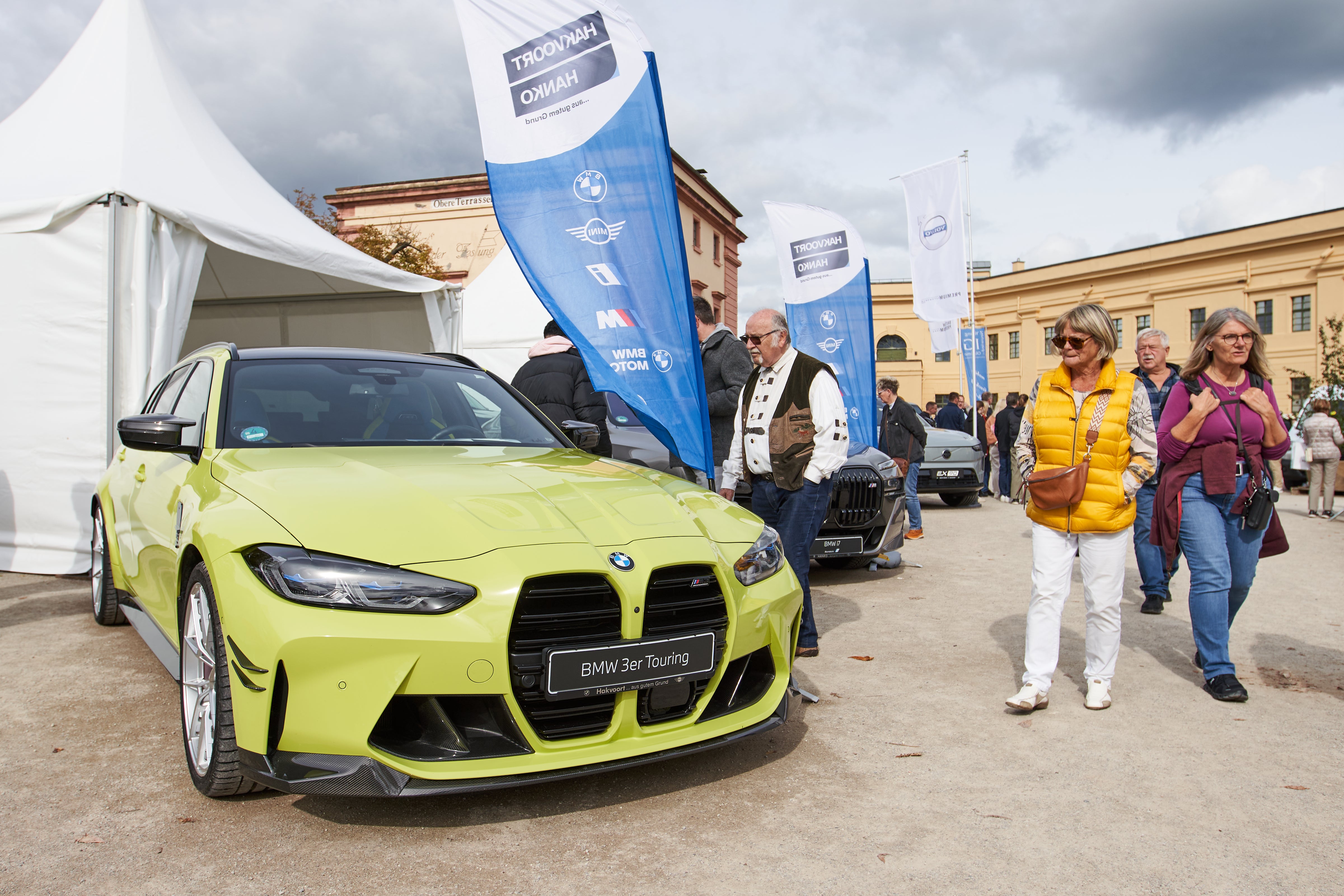 Eine Gruppe von Menschen spaziert an einem ausgestellten BMW 3er Touring in auffälligem Grün vorbei. 