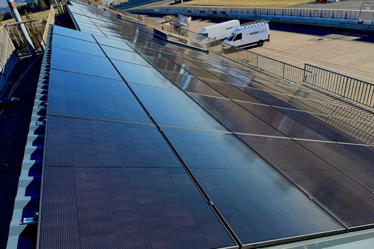 Großflächige Photovoltaikanlage auf einem Hallendach mit Servicefahrzeugen im Hintergrund.