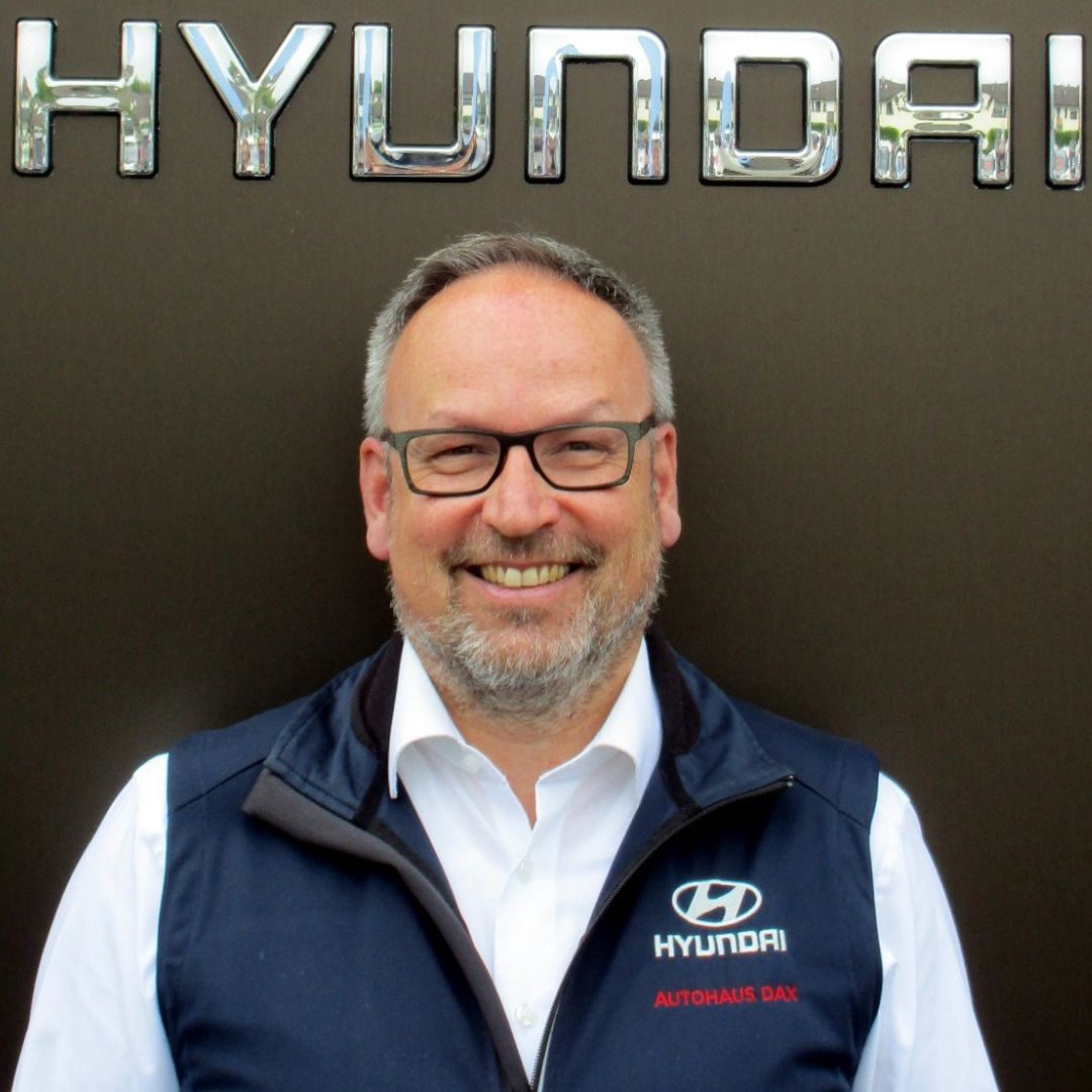 Ein Mann lächelt gerade in die Kamera, während er vor einem Hyundai-Logo steht.