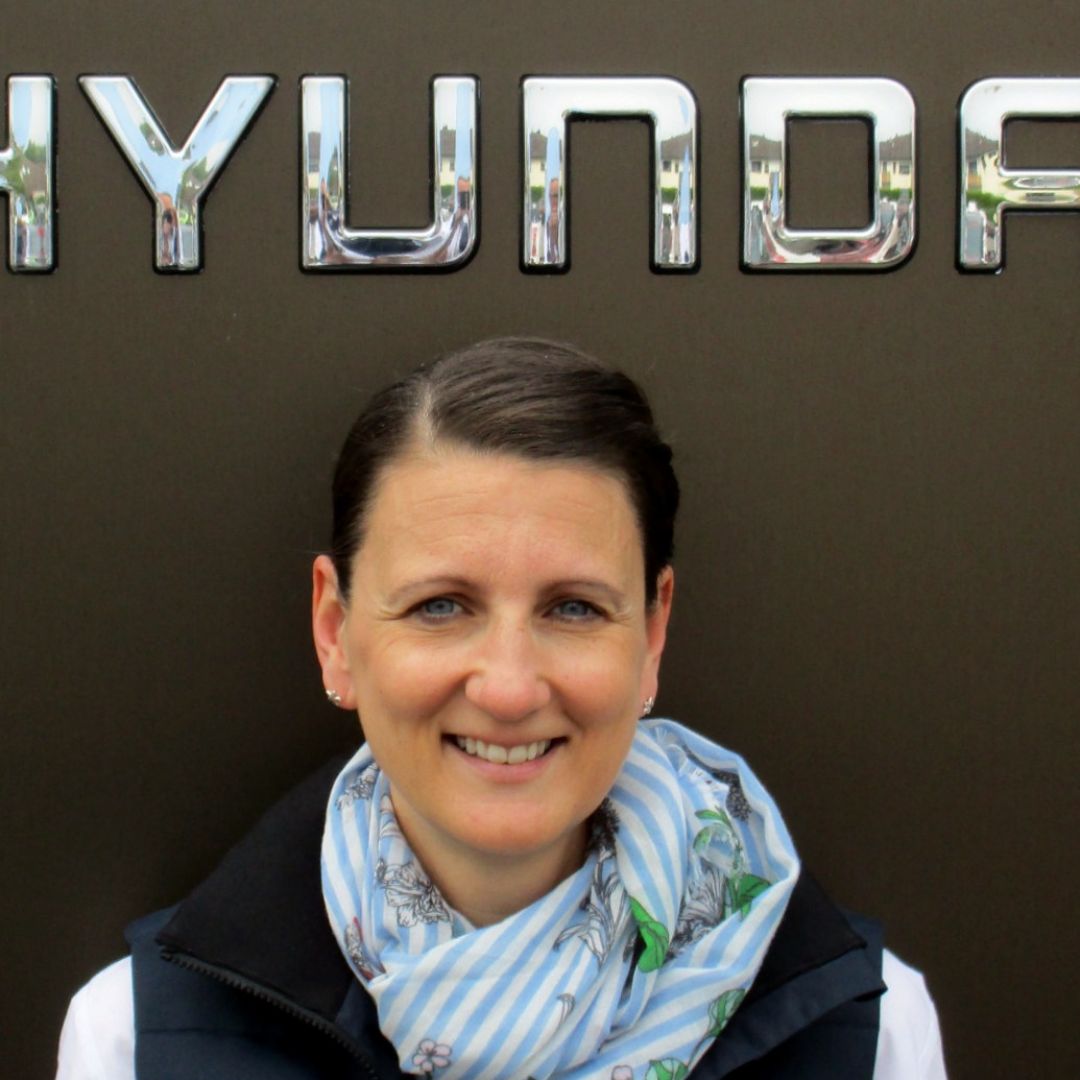 Eine Frau lächelt gerade in die Kamera, während er vor einem Hyundai-Logo steht.