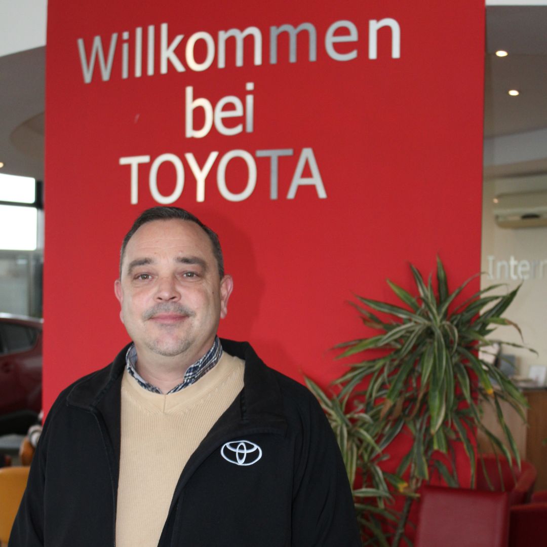 Ein Mitarbeiter vom Autohaus Hof steht vor einem Aufsteller mit der Aufschrift "willkommen bei Toyota".