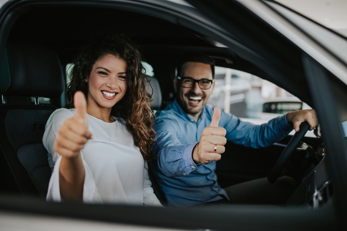 Ein mann und eine Frau sitzen in einem Auto und strecken einen Daumen in Richtung Kamera.