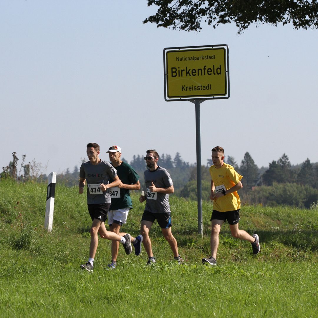 Eindrücke des Birkenfelder Firmenlaufs. Eine Gruppe läuft am Ortsschild "Birkenfeld" vorbei.