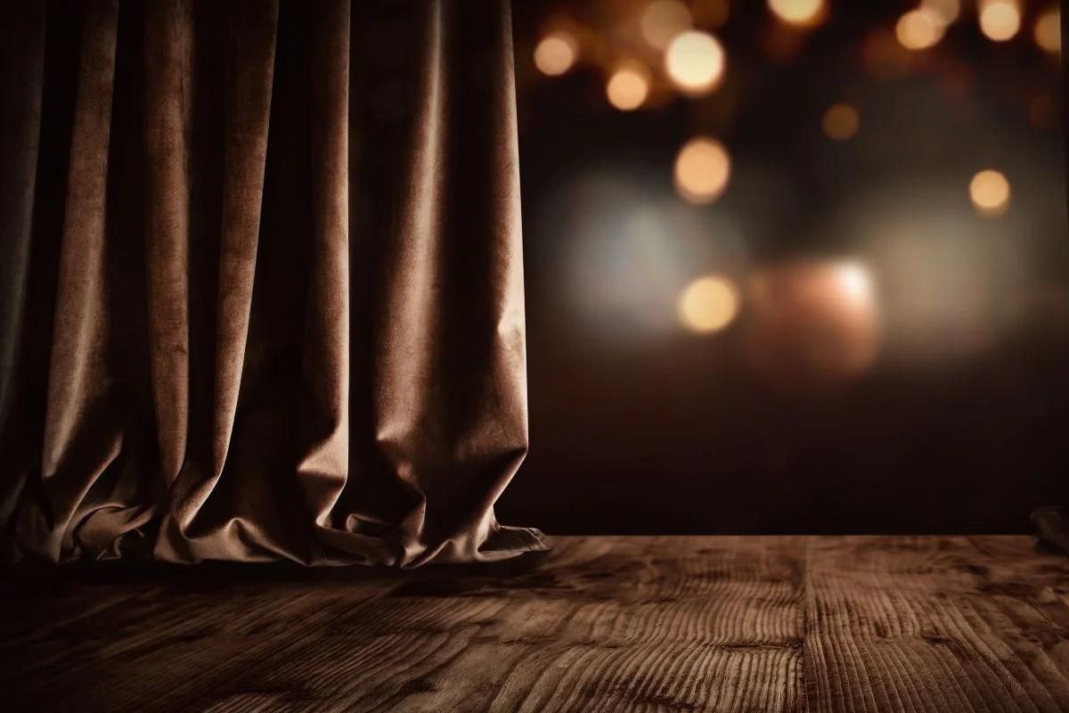 Ein schwerer Vorhang senkt sich auf die hölzerne Bühne eines Theaters.