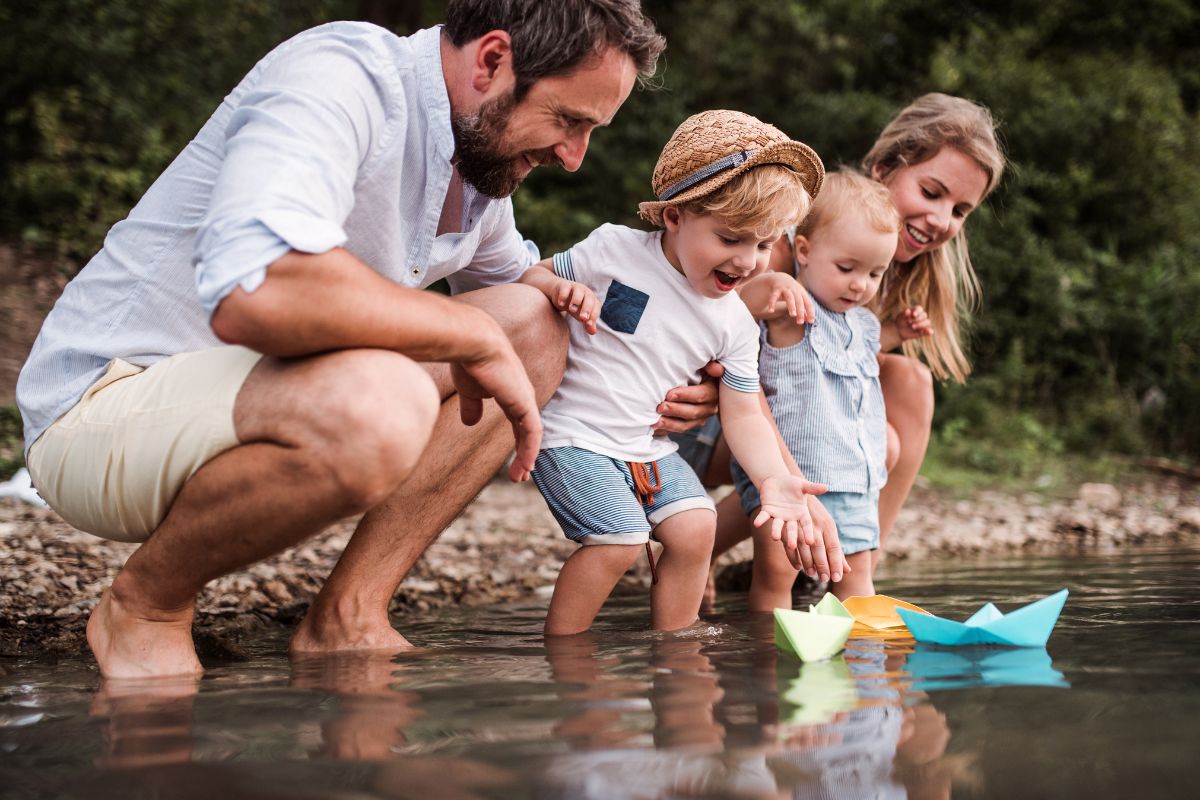 Eine Familie mit Kindern lässt Papierbote im Waser eines Sees schwimmen.
