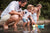 Eine Familie mit Kindern lässt Papierbote im Waser eines Sees schwimmen.