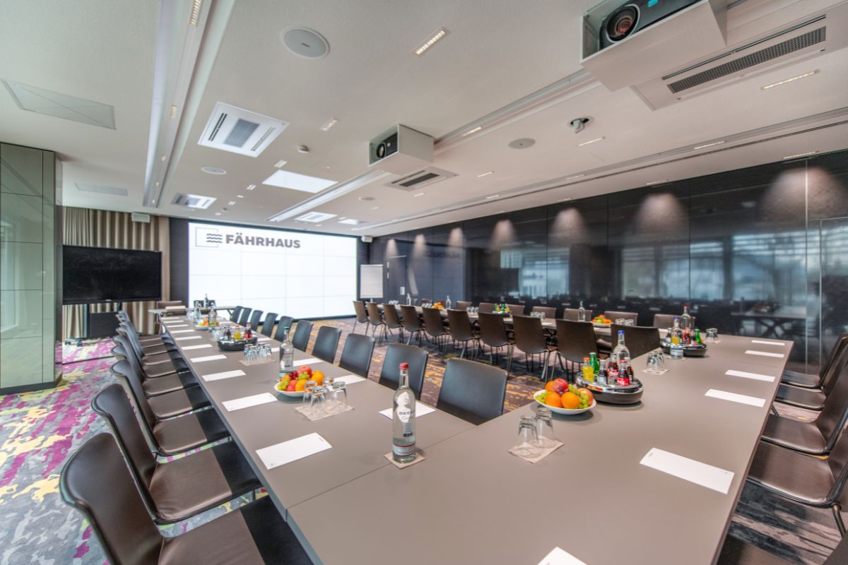 Im Konferenzraum des Fährhauses stehen auf den Tischen Obst und Getränke bereit, im Hintergrund ist ein Präsentationsbildschirm zu sehen.
