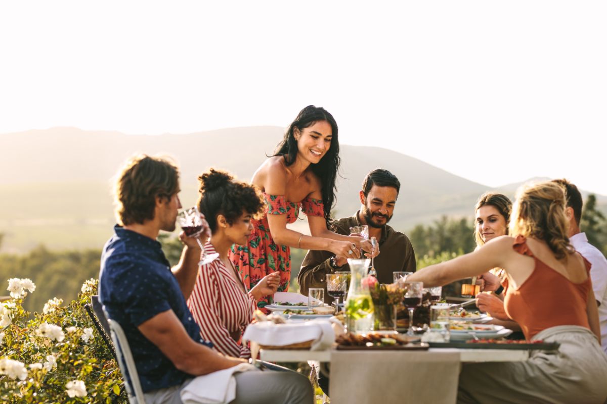 Gruppe von Freunden genießt ein gemeinsames Essen im Freien mit Blick auf eine hügelige Landschaft.