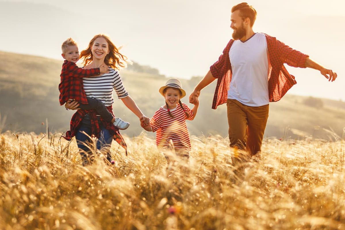 Fröhliche Familie mit zwei Kindern läuft durch ein goldenes Getreidefeld bei Sonnenuntergang.