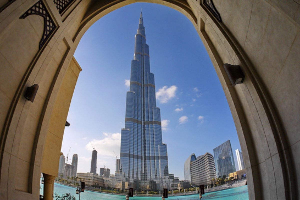 lick auf den Burj Khalifa, das höchste Gebäude der Welt, eingerahmt durch einen dekorativen Torbogen im Vordergrund. Das Bild zeigt die beeindruckende Höhe des Wolkenkratzers und einen klaren blauen Himmel darüber.