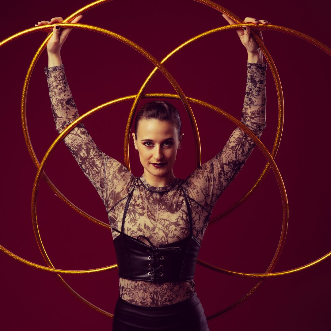 Artistin mit Hula-Hoop-Reifen vor bordeauxfarbenem Hintergrund.