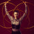 Artistin mit Hula-Hoop-Reifen vor bordeauxfarbenem Hintergrund.