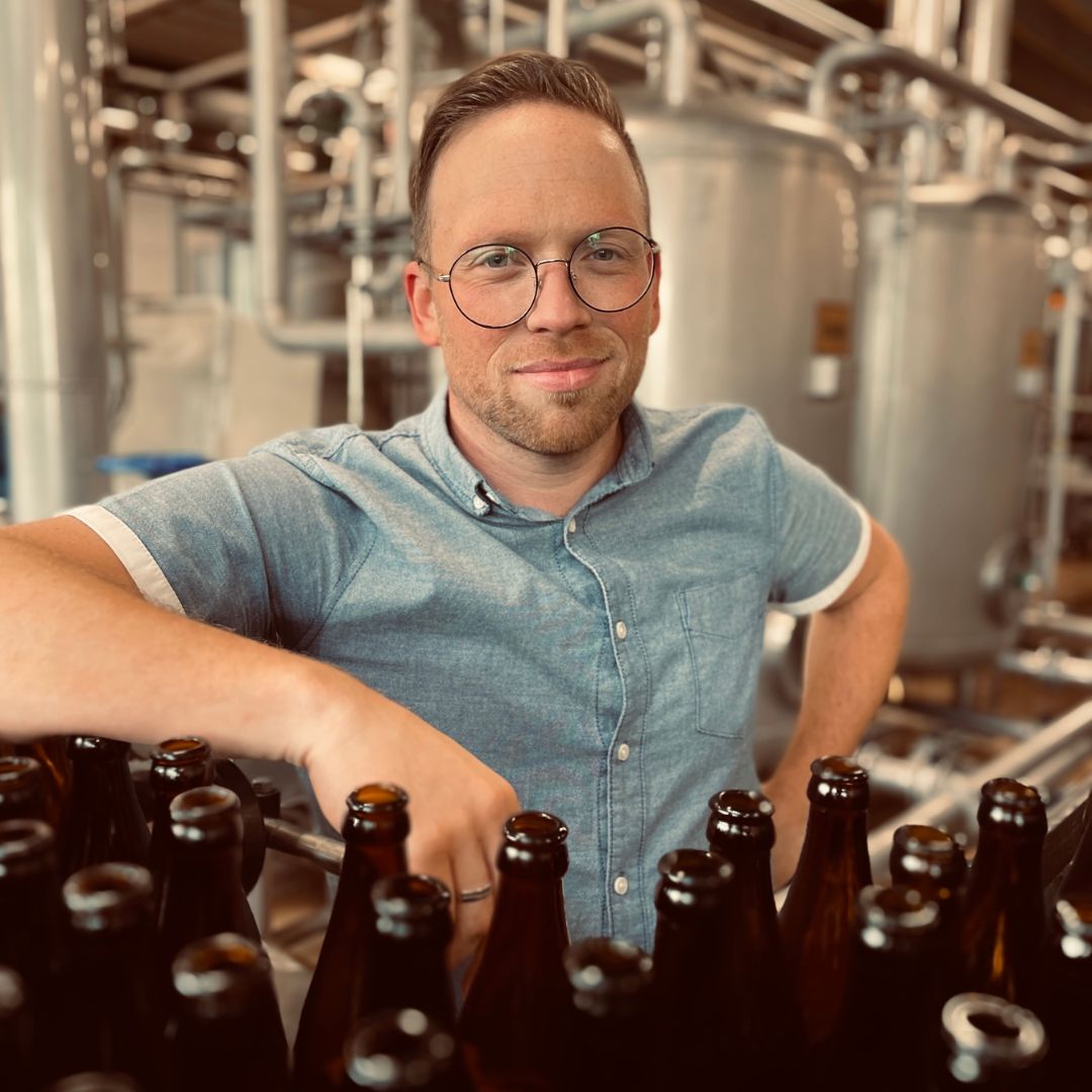 Ein Mann steht stolz vor den Bierflaschen der hachenburger Brauerei.