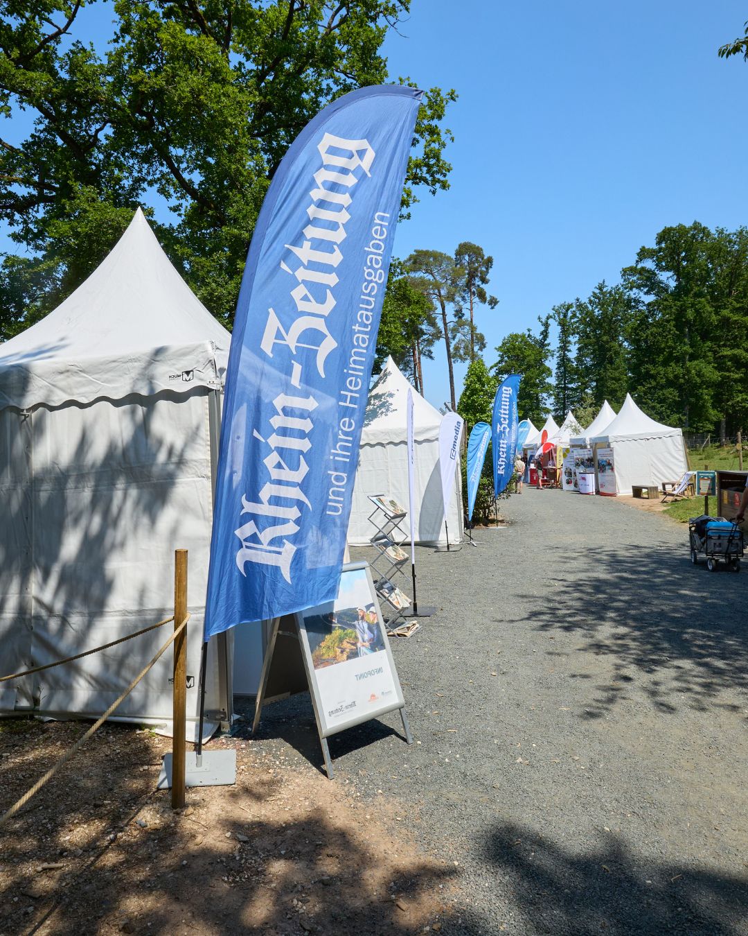 Ausstellerzelte und Informationsstände bei der Jobmesse „Jobs im Park“. Im Vordergrund eine Fahne der Rhein-Zeitung, entlang eines Weges reihen sich weitere Messestände.