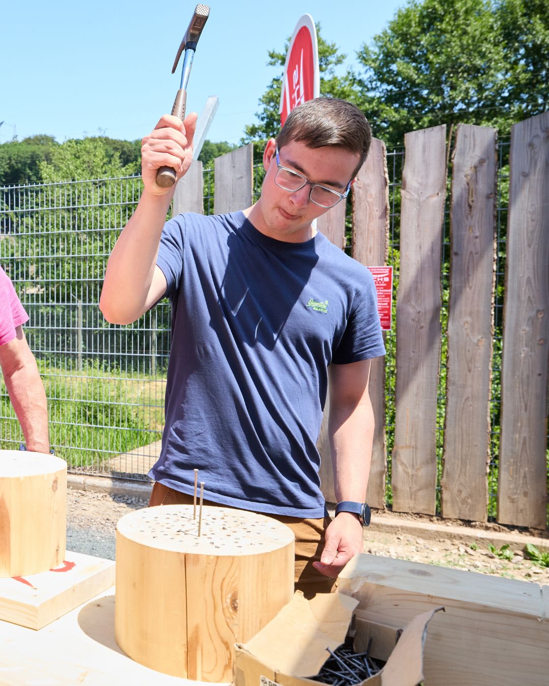 Person schlägt bei der Jobmesse „Jobs im Park“ mit einem Hammer Nägel in einen Holzblock und testet handwerkliches Geschick an einem Mitmachstand.