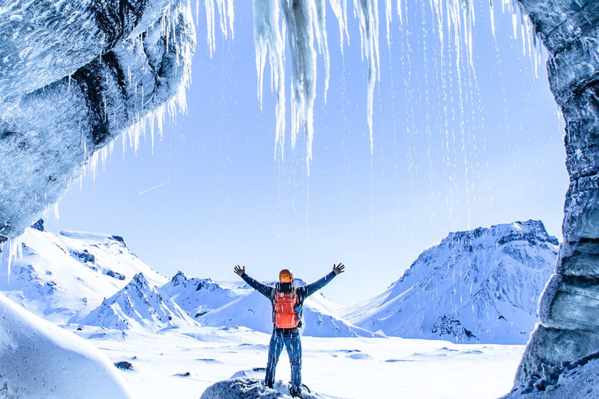 Ein Mann steht under riesigen Eiszapfen ind Winterkleidung. Im Hintergrund ist ein weißes Schneefeld zu sehen und die Sonne scheint.