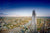 Ein atemberaubender Blick auf den Shard, eines der höchsten Gebäude in London, der sich über die Stadt erhebt. Im Hintergrund fließt die Themse, und die Tower Bridge ist zu sehen, zusammen mit den umliegenden Gebäuden und Straßen. Die Skyline erstreckt sich bis zum Horizont unter einem klaren blauen Himmel.