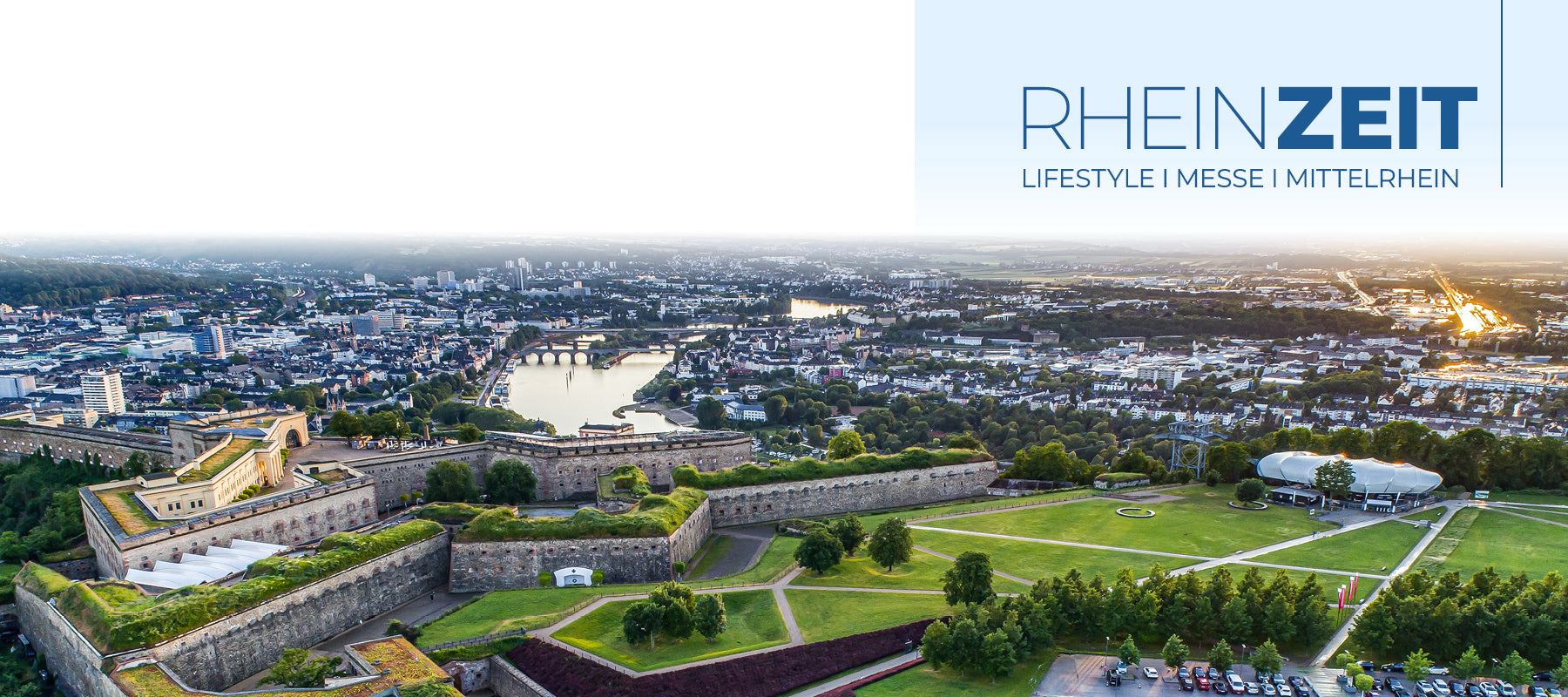 Ausblick von der Festung Ehrenbreitstein auf das deutsche Eck in Koblenz bei Sonnenuntergang. Rechts ist das blaue Logo dr "RHEINZEIT"-Messe abgebildet.