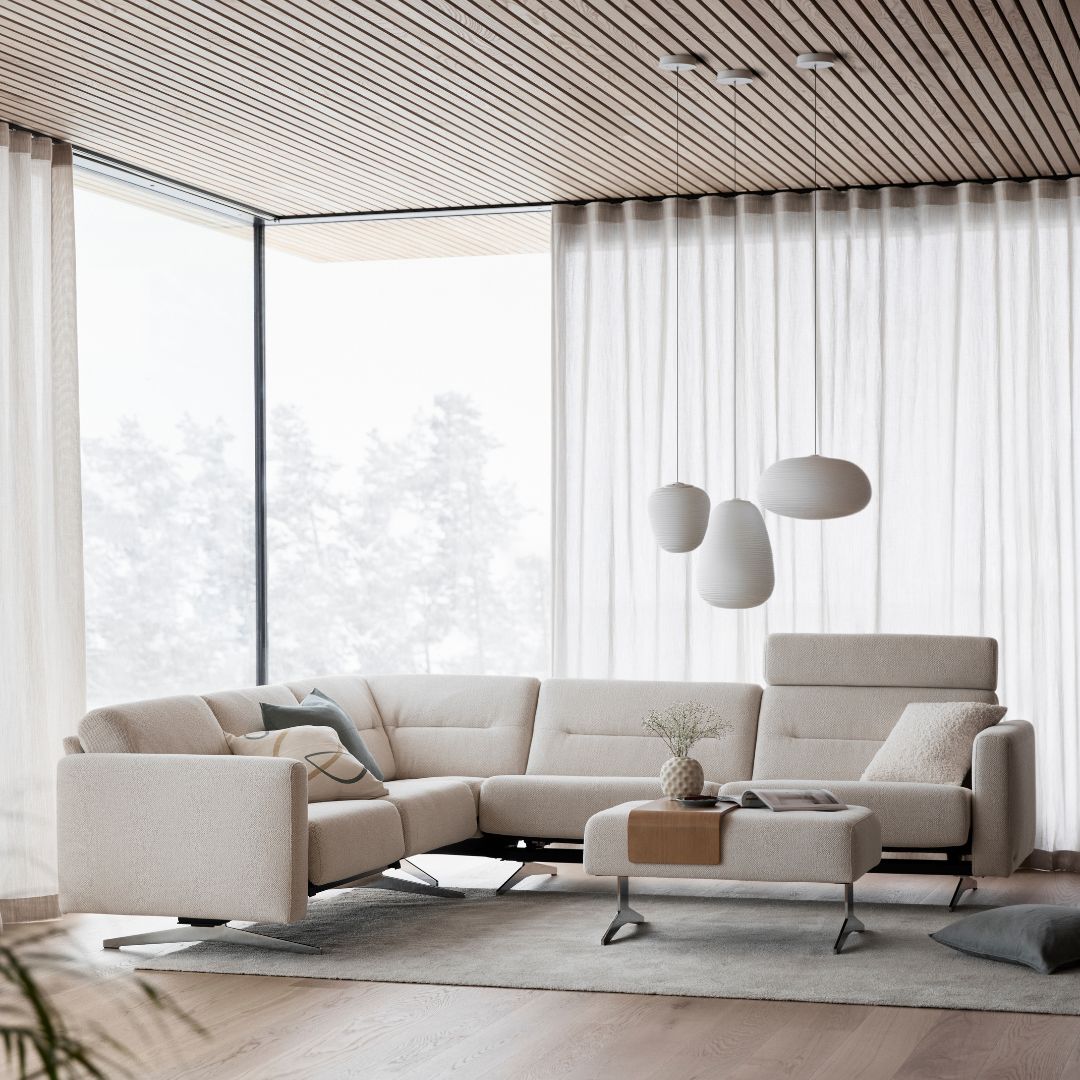 Ein modernes Wohnzimmer, mit deckenhohen Fenstern, einer Beigen Couch mit passendem Beistelltisch und einer verspielten Lampe. Alles ist in passenden Beigetönen gehalten.