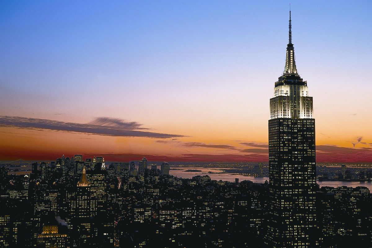 Das berühmte Empire State Building, das sich majestätisch gegen den farbigen Himmel des Sonnenuntergangs abhebt, ist von weiteren Wolkenkratzern in der New Yorker Skyline umgeben.