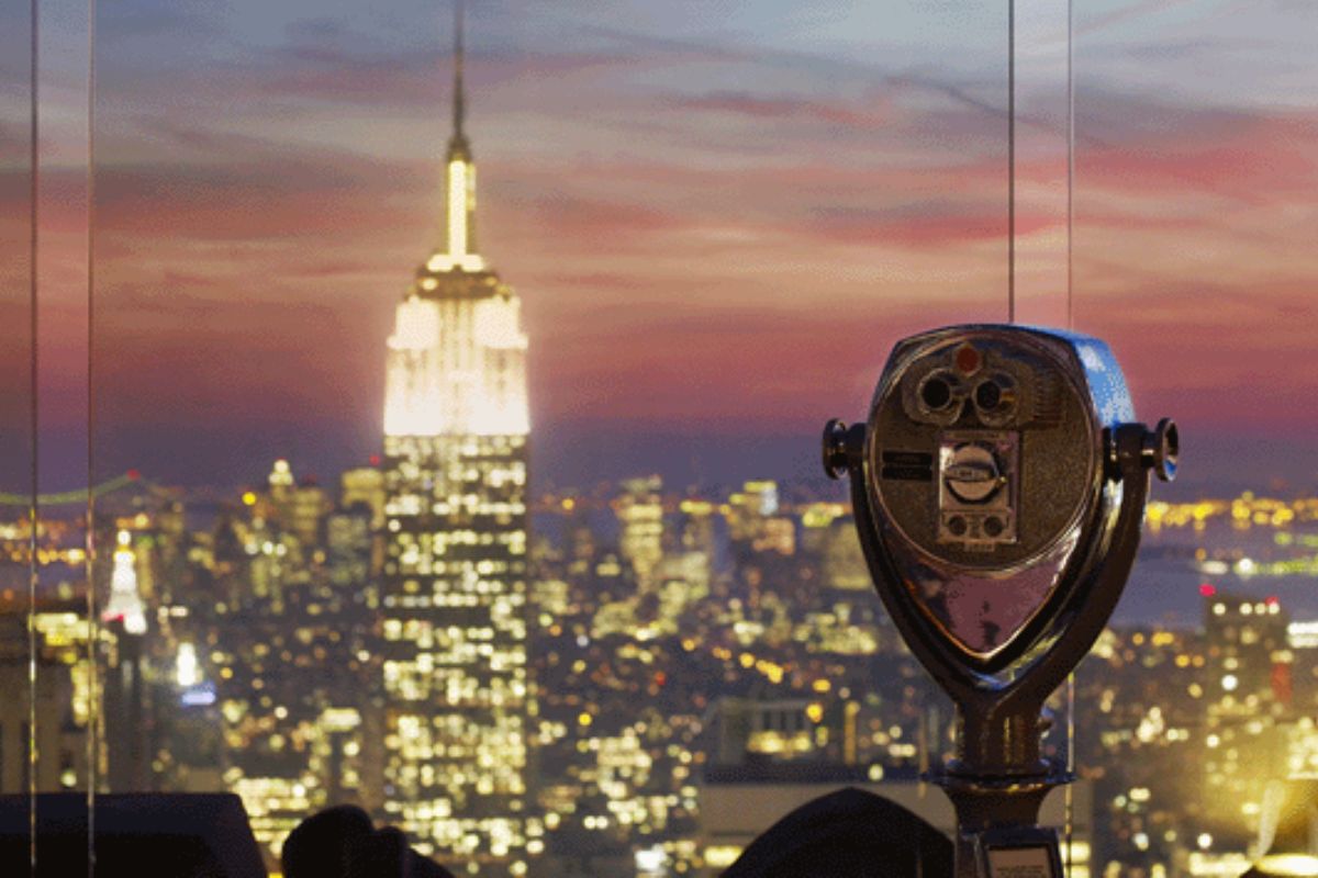 Ein Fernglas auf der Aussichtsplattform am Top of the Rock bietet einen klaren Blick auf das nächtliche New York City, mit dem hell erleuchteten Empire State Building im Hintergrund.