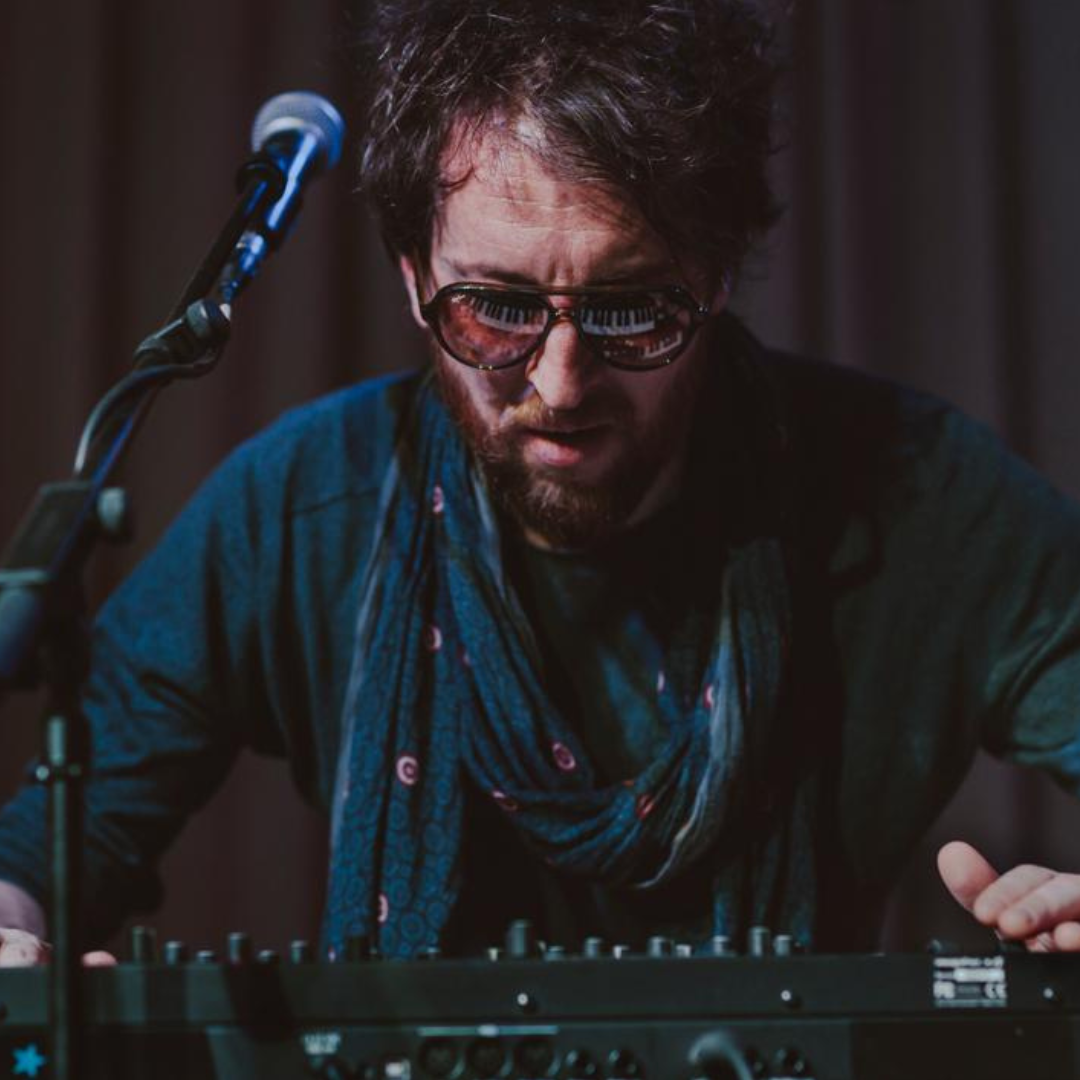 Ein Mann, der ein Mischpult bedient. In seiner Sonnenbrille spiegelt sich ein Keyboard