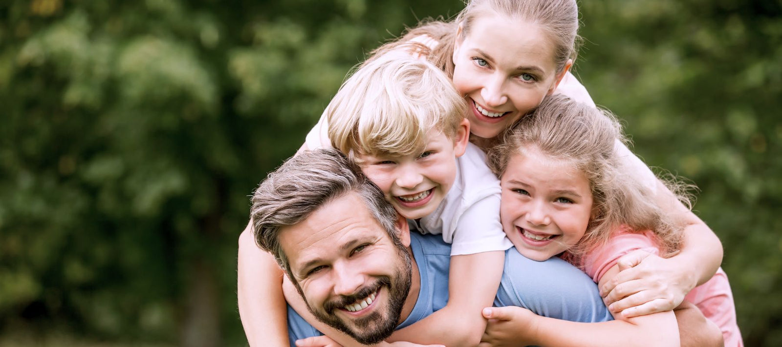 Eine glückliche 4-Köpfige Familie im grünen die lächelnd in Richtung Kamera schauen.