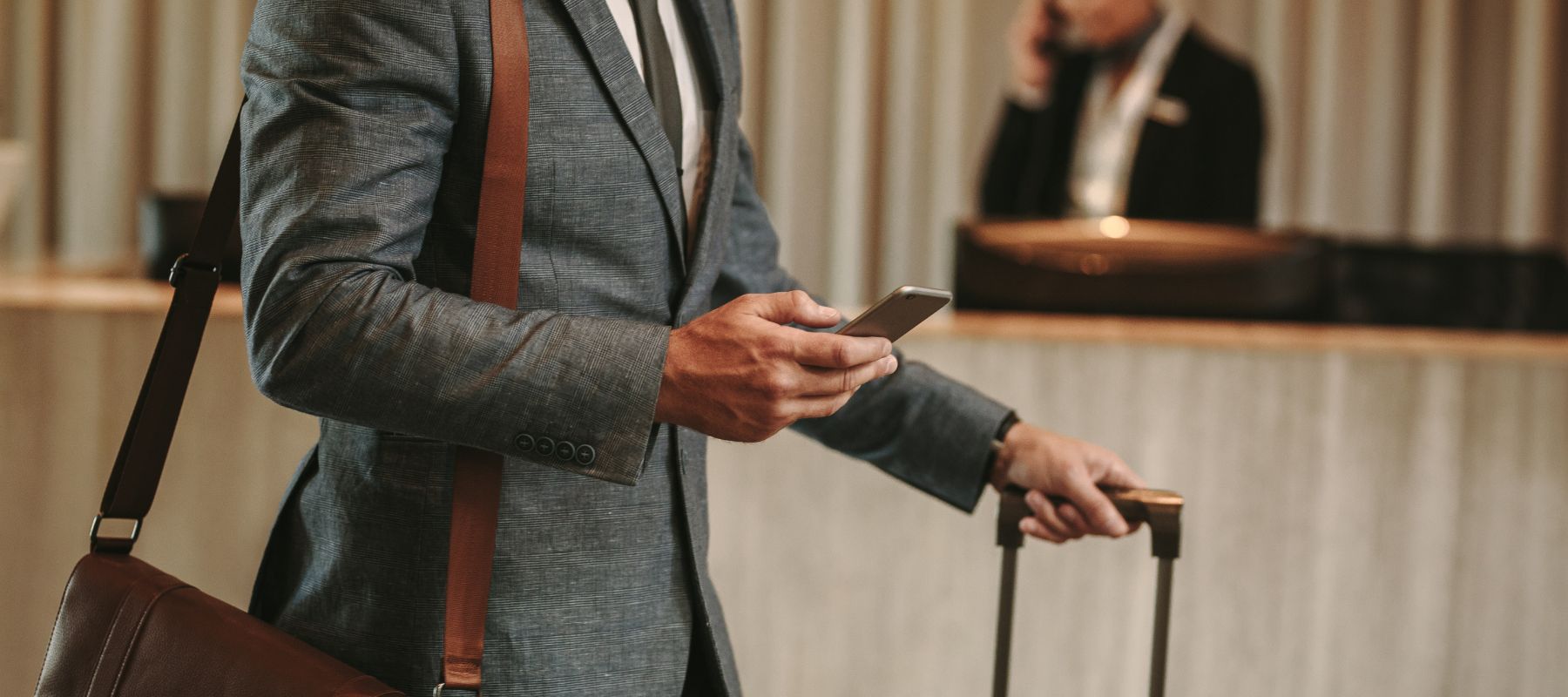 Ein Mann im Anzug läuft durch ein Hotel und schaut auf sein Smartphone.