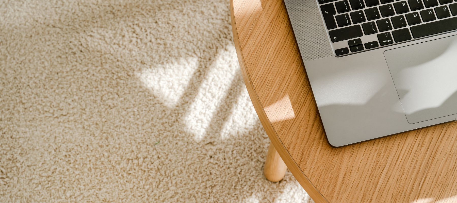 Ein Laptop auf einem Holztisch, der auf einem Creme farbenem Teppich steht