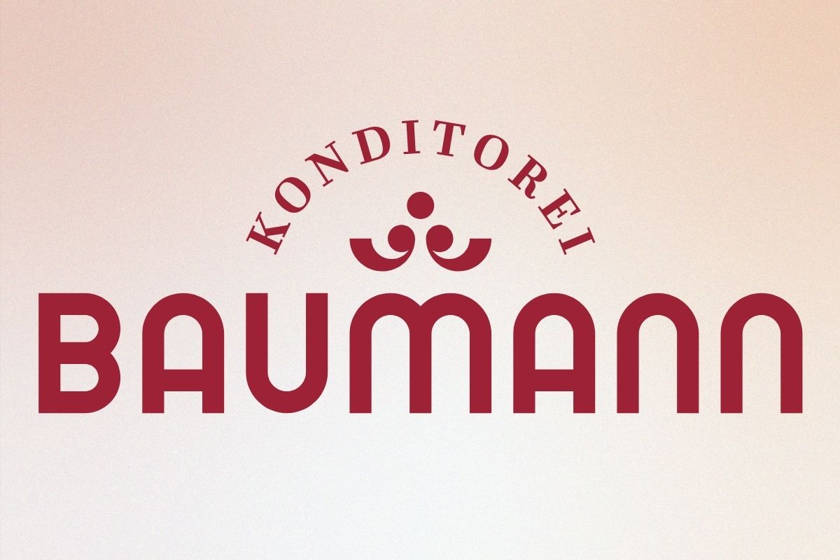 Das bordeauxrote Logo der Konditorei Baumann auf einem Hintergrund, der einen beigen Farbverlauf darstellt.