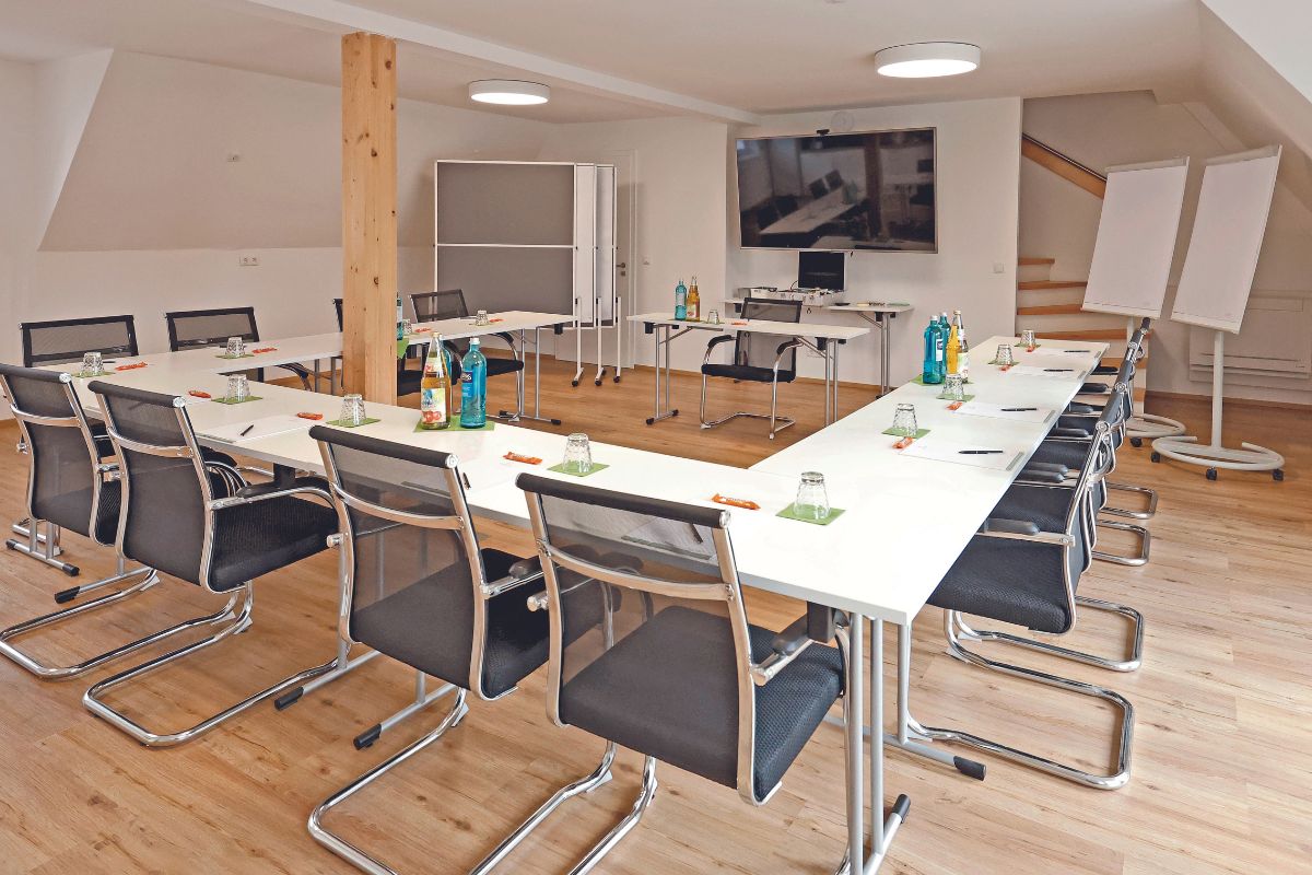 Ein Raum der für eine Konferenz eingedeckt ist. In einer U-Form mit einem Tisch am offenem Ende.