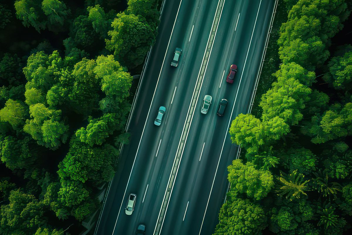 Luftaufnahme einer Autobahn, die durch dichte grüne Wälder verläuft, was die Verbindung von Verkehr und Natur betont.