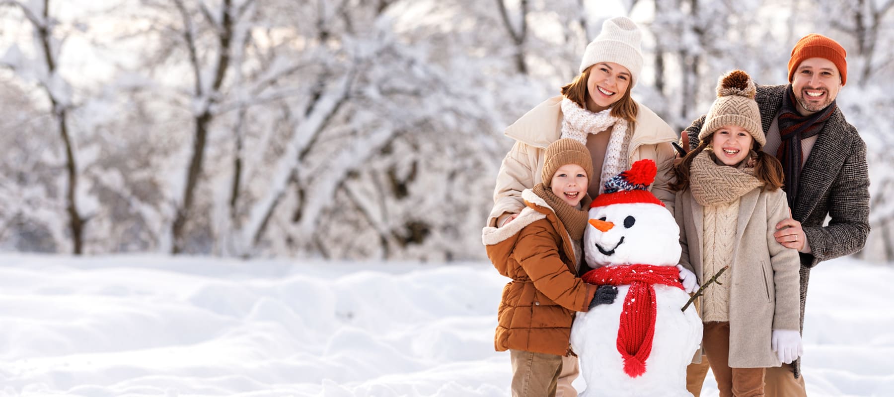 Eine Familie steht auf einem Feld, das von Schnee bedeckt ist. Alle haben Spaß und haben zusammen einen Schneemann gebaut, der einen roten Schal und eine rote Mütze trägt.