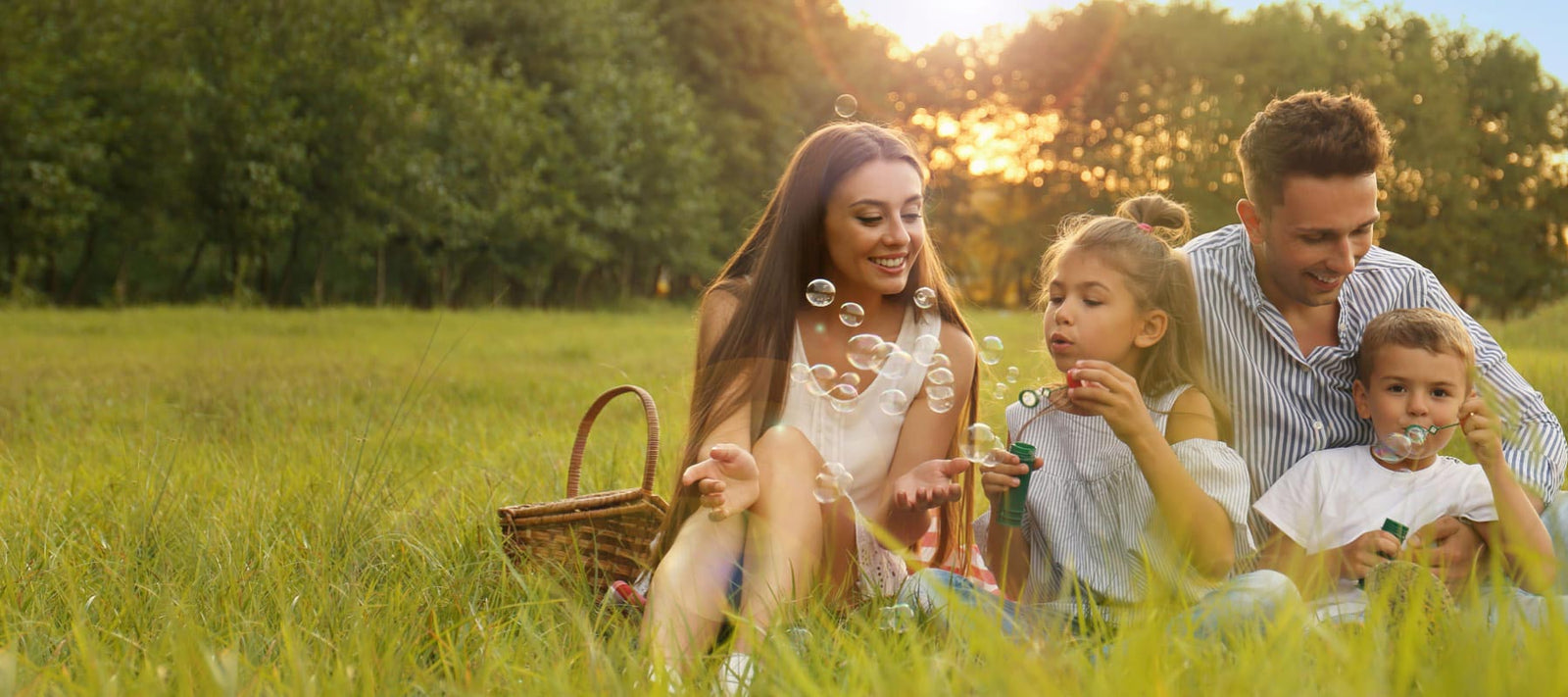 Eine Familie mit zwei Kindern sitzt auf einer Wiese. Die Kinder machen Seifenblasen.